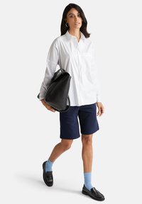 Camicia bianca con bottoni, pantaloni corti blu navy, borsa nera, mocassini neri, calzini blu. Tessuto morbido, vestibilità rilassata, orlo arrotondato.
