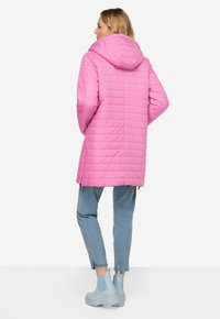 Abrigo largo rosa acolchado con capucha, con costuras verticales y aberturas laterales. Combinado con vaqueros azul claro y botas de tobillo a juego.