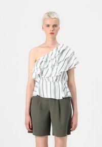 Bluză cu un umăr, dintr-un material alb cu dungi verzi și volane. Asortată cu pantaloni scurți de culoare verde măsliniu, având un design peplum.