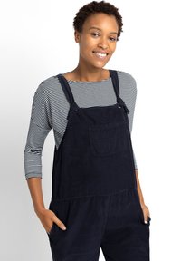 Marineblauwe corduroy-overalls met verstelbare banden, een voorkant pocket en een relaxte pasvorm, gecombineerd met een zwart-wit gestreept langemouwen shirt.