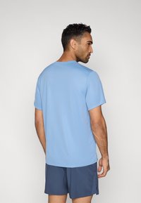 Világoskék, rövid ujjú póló környakú kivitelben; sötétkék rövidnadrággal párosítva. Simább anyag, minimális díszítéssel, alkalmi viseletre alkalmas.