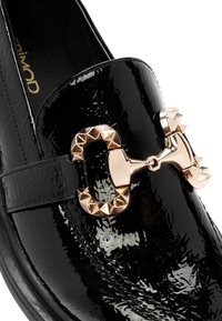 Schwarzer Lackleder-Slipper mit goldfarbenen Nietenakzenten und einer glatten Oberfläche sowie einem runden Zehenbereich.