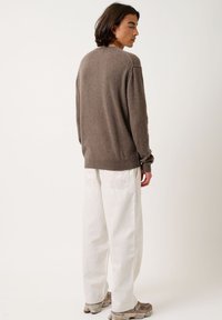 Brun ulltröja med rund halsringning och sänkta axlar; stylar med löst sittande vita byxor och beiga sneakers. Enkel, strukturerad design.