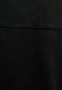 Tejido de punto negro con una textura suave y un brillo sutil. Cuenta con una costura horizontal en la parte superior para darle estructura.