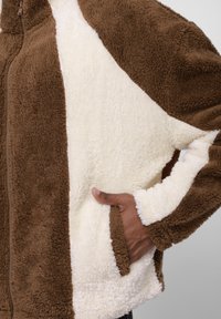 Brun og cremefarvet blød fleecejakke med lynlåslukning, der har et farveblokdesign og sidelommer. Teksturen er blød og plyssede.