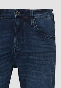 Jean en denim bleu foncé avec bouton frontal, fermeture éclair, passants pour ceinture et détails de poche latérale.