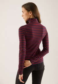 Langermet turtleneck i marineblått med horisontale røde striper. Har tettsittende passform og myk stoff, med lange ermer og høy krage.