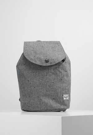 Gray fabric backpack with flap and button closure, small black speckles, and a rectangular brand patch on the lower right front.