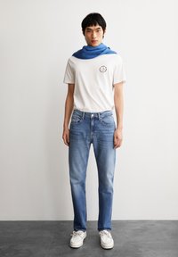 Witte T-shirt met rond logo, blauwe sjaal, lichtblauwe jeans en witte schoenen. Casual outfit met een eenvoudig ontwerp en zachte texturen.