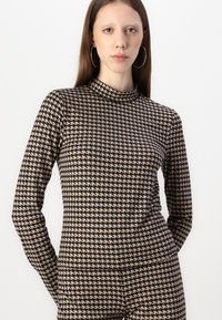 Langarmtop in een houndstoothpatroon, met een hoge hals, in zwart en beige. De stof lijkt soepel met een getailleerd ontwerp.