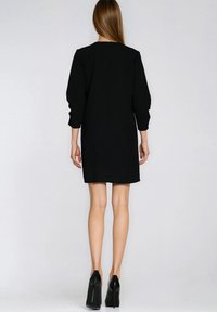 Czarna sukienka z długimi bufkami, prostą sylwetką oraz detalem z tyłu - zamkiem błyskawicznym. Noszona z czarnymi czółenkami na wysokim obcasie. Gładkie wykończenie tkaniny.