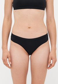 Woman wearing black underwear and black sports bra, shown from mid-thigh to upper abdomen against a plain white background.