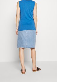 Modrá bezrukávová blůza spárovaná se světle modrou džínovou sukní s třepeným lemem, nošená s černými sandály, viděná zezadu.