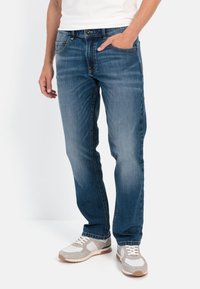 Blaue Denim-Jeans mit geradem Bein, Fronttaschen und dezenten Verwaschungen, kombiniert mit neutral gefärbten Sportschuhen.