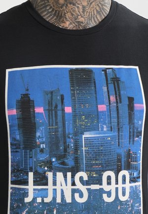 Czarny t-shirt przedstawiający panoramę miasta z wysokimi nowoczesnymi drapaczami chmur o zmierzchu oraz tekst J.JNS 90 nadrukowany pod obrazem.
