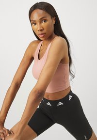 Ružičasti sportski crop top s dizajnom u obliku slova V, uparen s crnim biciklističkim šortsem koji ima bijelu logo traku na struku. Glatka tekstura tkanine.