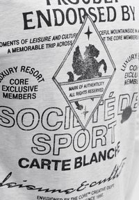 Textový dizajn na látke obsahujúci frázy o exkluzívnom členstve v luxusnom rezorte, emblém leva a slová ako "Société de Sport" a "Carte Blanche".