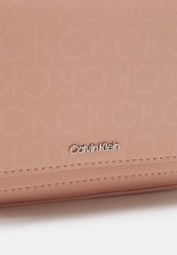 Portafoglio rosa testurizzato con logo in rilievo e il logo Calvin Klein in argento. Il materiale liscio con cuciture ben definite aggiunge dettagli.