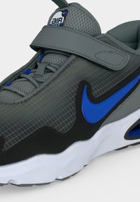 Γκρι αθλητικό παπούτσι Nike Air Max με μπλε σήμα, κλείσιμο με λουράκι, επάνω μέρος από δίχτυ και άσπρη σόλα σε κοντινή γωνία.