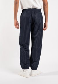 Navy blue track pants with elastic waistband and cuffs, made of lightweight, smooth material. Feature a relaxed fit and side pockets.