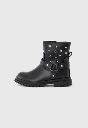 Stivali ankle in pelle nera con borchie argentate, una fascia attorno alla parte centrale e una suola in gomma texture. Cerniera laterale per un facile accesso.