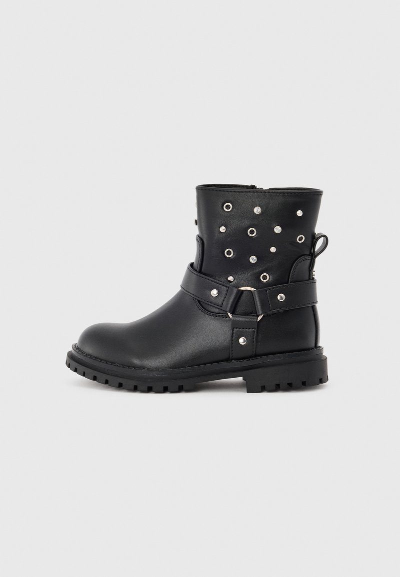 Botas de tobillo de cuero negro con tachuelas plateadas, una correa alrededor de la parte media y una suela de goma texturizada. Cierre lateral para un fácil acceso.