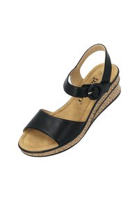 Sandalo in pelle nera con una larga fascia e una cinghia alla caviglia regolabile, montato su una suola a zeppa beige texturizzata. Suola interna morbida e imbottita visibile.