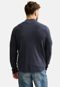 Marineblauer Strickpullover mit rundem Ausschnitt und langen Ärmeln, mit einer glatten Textur und einem schlichten Design, getragen über hellblauen Jeans.