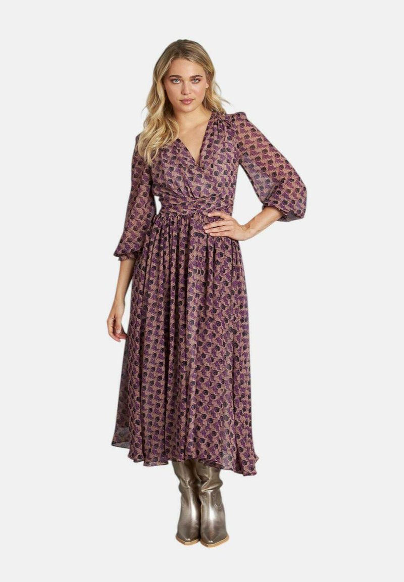 Langes lila Wickelkleid mit Blumenmuster, Dreiviertelärmel, Taillengürtel und fließendem Rock. Kombiniert mit kniehohen metallisch silbernen Stiefeln.