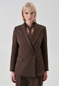 Blazer marrone a righe con rever a lancia, chiusura con un bottone e due tasche frontali. Abbinato a cravatta e pantaloni coordinati.