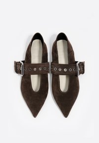 Mocasines de ante marrón con punta afilada, que presentan una amplia correa adornada con ojetes de plata y un detalle de hebilla metálica.