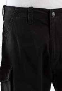 Pantalones cargo negros con tejido texturizado, que cuentan con múltiples bolsillos, un cierre de botón y lazos para cinturón. Acabado suave con detalles de costura robusta.