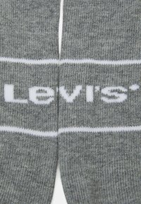 Calzini in cotone grigi con una striscia orizzontale bianca e il logo "Levi's" in testo bianco sulla superficie. Texture liscia, forma standard per calzini.