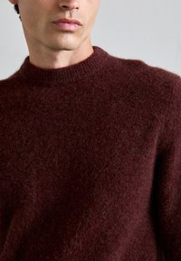 Burgundiszínű gyapjú pulóver, kerek nyakkivágással. Az anyag puha és textúrált, diszkrét, bolyhos befejezéssel rendelkezik.