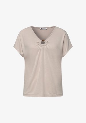 Blouse beige à manches courtes avec col en V, détail froncé et anneau circulaire en écaille de tortue à l'encolure.