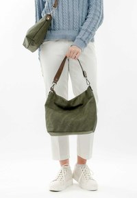 Grüne Canvas-Schultertasche mit Ledertrageriemen, weicher Textur, lässigem Design und einem dezenten Logo auf der Vorderseite. Begleitet von einer passenden kleineren Tasche.