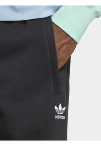 Black athletic joggers with ribbed texture and side pockets. Features white Adidas trefoil logo on the lower leg.