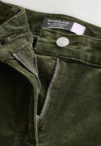 Zöld kordbársony farmernadrág magas derekú, laza bootcut fazonnal, fém cipzárral, gombos záródással és márkacímkével a derékpánton.