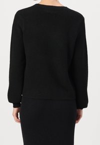 Černý žebrovaný svetr s dlouhými rukávy, kulatým výstřihem a volnějším střihem. Materiál působí měkce s texturovaným povrchem. Zobrazen pohled zezadu.