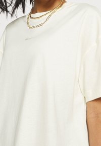 Vit kortärmad t-shirt i mjuk bomull, med en minimalistisk design och en subtil logotyp samt lager av guldkedjor.