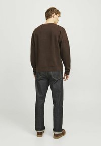 Felpa marrone e jeans scuri. La felpa presenta una vestibilità comoda con maniche lunghe e colletto a girocollo; i jeans hanno un taglio classico con cuciture a contrasto.