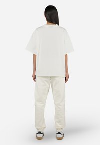 Oversized white cotton t-shirt with a crew neck and short sleeves, paired with white sweatpants and casual sneakers.