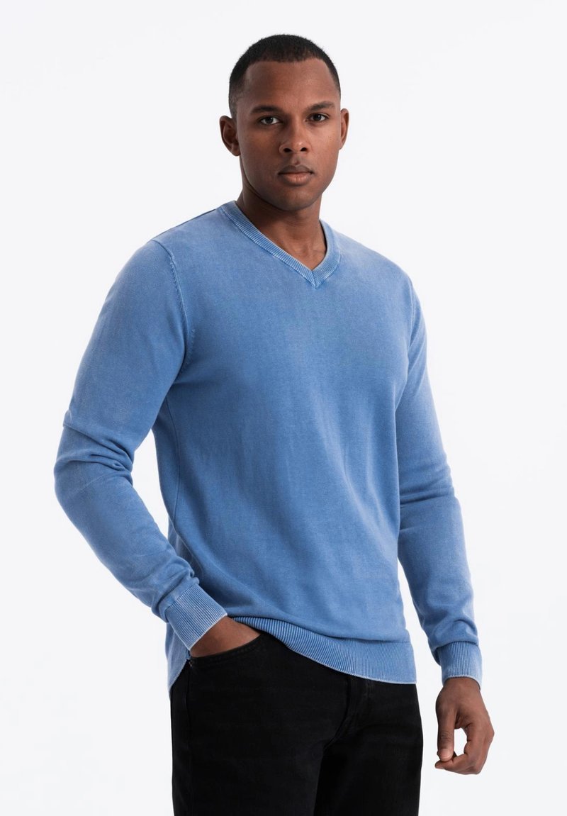 Suéter de cuello en v azul claro hecho de un material suave, con mangas largas y puños y dobladillo acanalados. Llevado sobre pantalones negros.