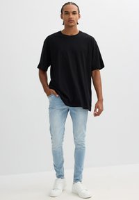 Camiseta negra oversized, jeans ajustados de color azul claro, zapatillas blancas. Material de algodón suave, mangas cortas, diseño simple, ajuste casual.