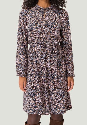 Mujer con un vestido floral de manga larga hasta la rodilla, con cinturón en la cintura y escote con abertura, combinado con botas marrones.