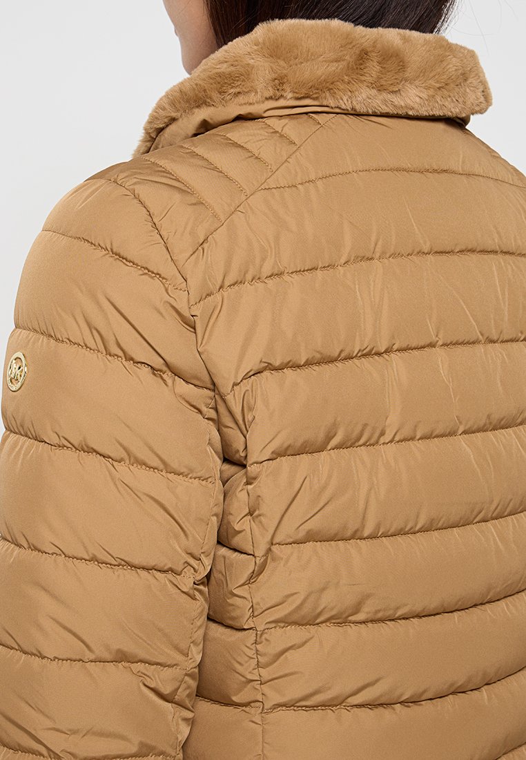Puffermantel in hellbraun mit horizontalen Nähten, Kunstfellkragen und einem Logo-Akzent. Glatte Textur, leichtes Design.