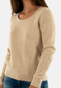 Maglione a maglia beige con scollatura rotonda, polsini e orlo ribattuti, e una texture morbida. Abbinato a jeans in denim blu.