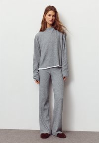 Pulover gri texturat cu guler înalt și mâneci lungi, asortat cu pantaloni evazați gri, din același material. Ambele sunt confecționate dintr-un țesut moale și confortabil.