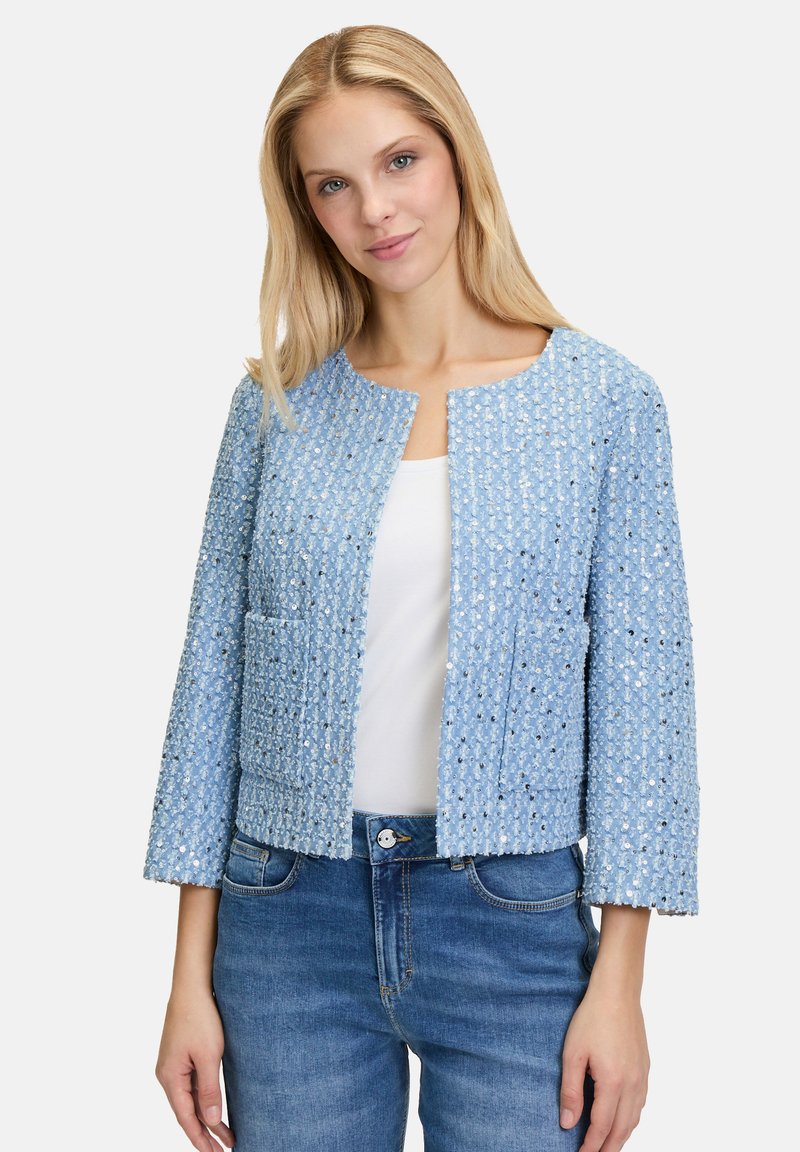 Veste texturée bleu clair avec des manches trois quarts, un décolleté carré et des poches avant. Le matériau tissé présente un motif subtil.