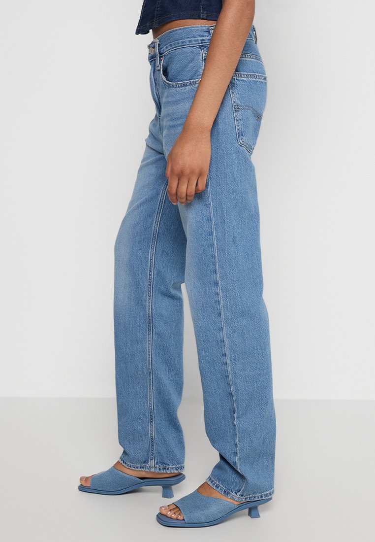 Hellblaue, weit geschnittene Jeans mit hoher Taille und Fronttaschen, kombiniert mit passenden blauen offenen Sandalen mit Absatz.